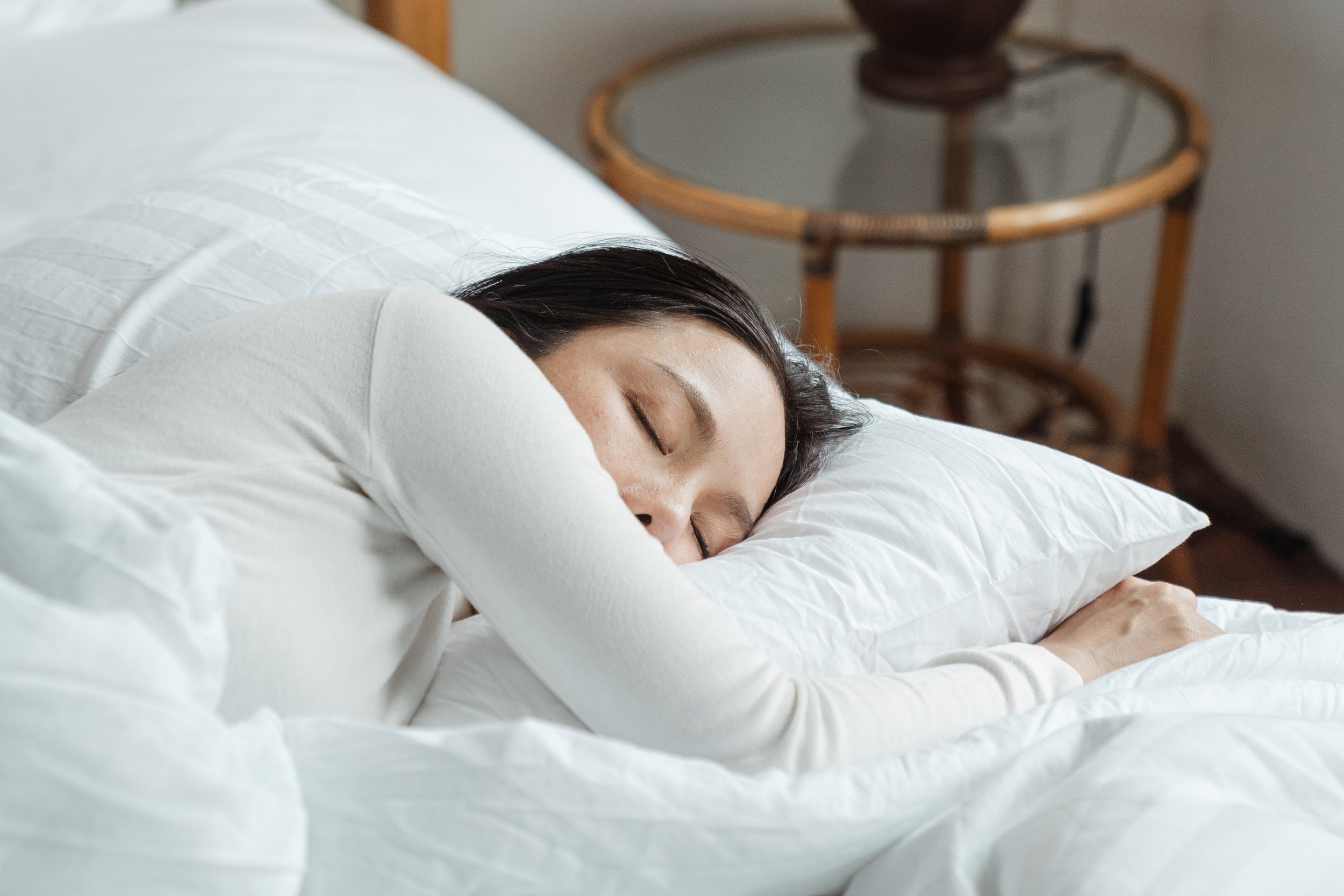 Woman peacefully sleeping in a cozy bedroom, representing the benefits of natural sleep aids and supplements for a restful night’s sleep.